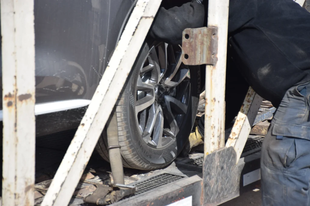 Primer plano de la rueda de un vehículo sujeta con correas sobre la plataforma de un camión porta-autos