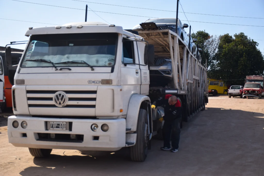 Camión Volkswagen porta-autos cargado con varios vehículos, con un operario de Movaris revisando el equipo antes de partir