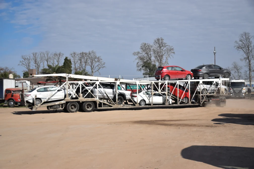 Camión porta-autos de Movaris circulando por camino de tierra con varios vehículos cargados y levantando polvo